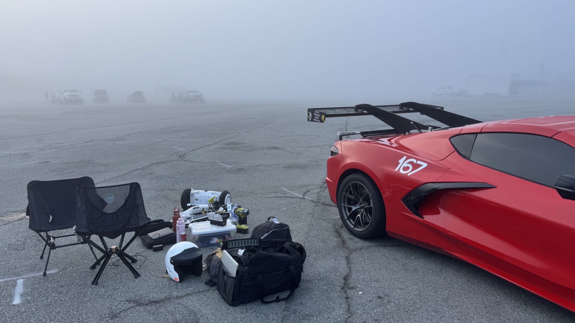 Red C8 track car with rear wing in the paddock at dawn, gear laid out